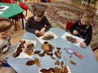 Dzieci wyklejają legowisko jeża zasuszonymi liśćmi